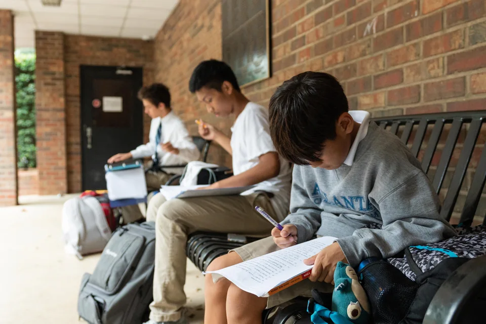 Students reading and writing on a covered outdoor bench at ACA