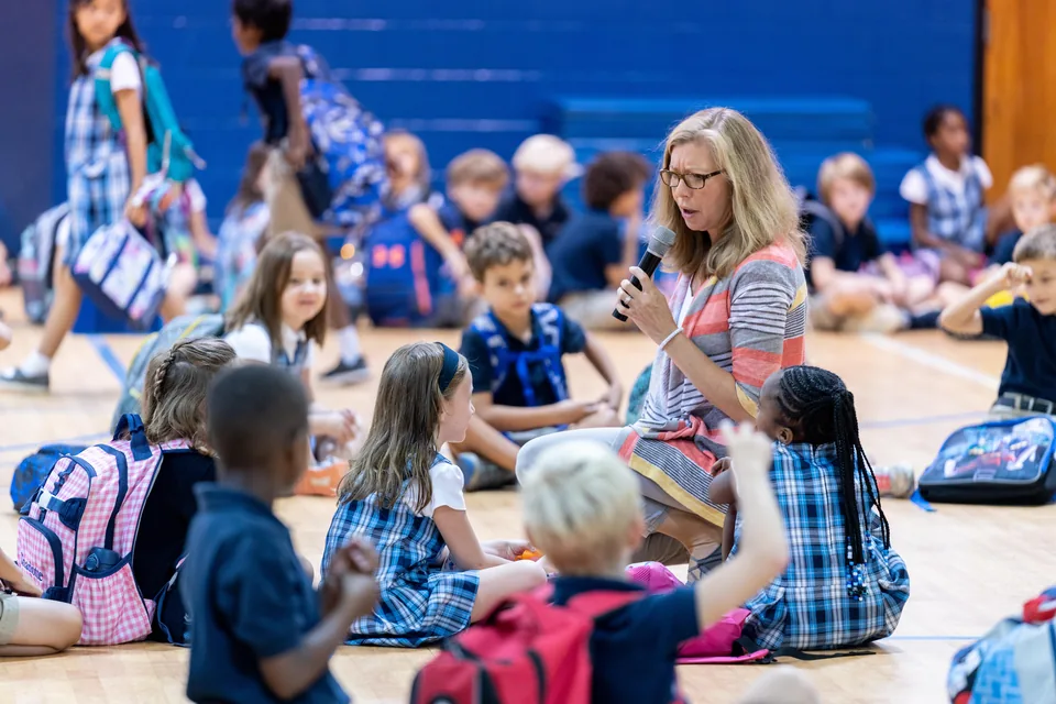 Adult speaking with children seated together in a gym at ACA